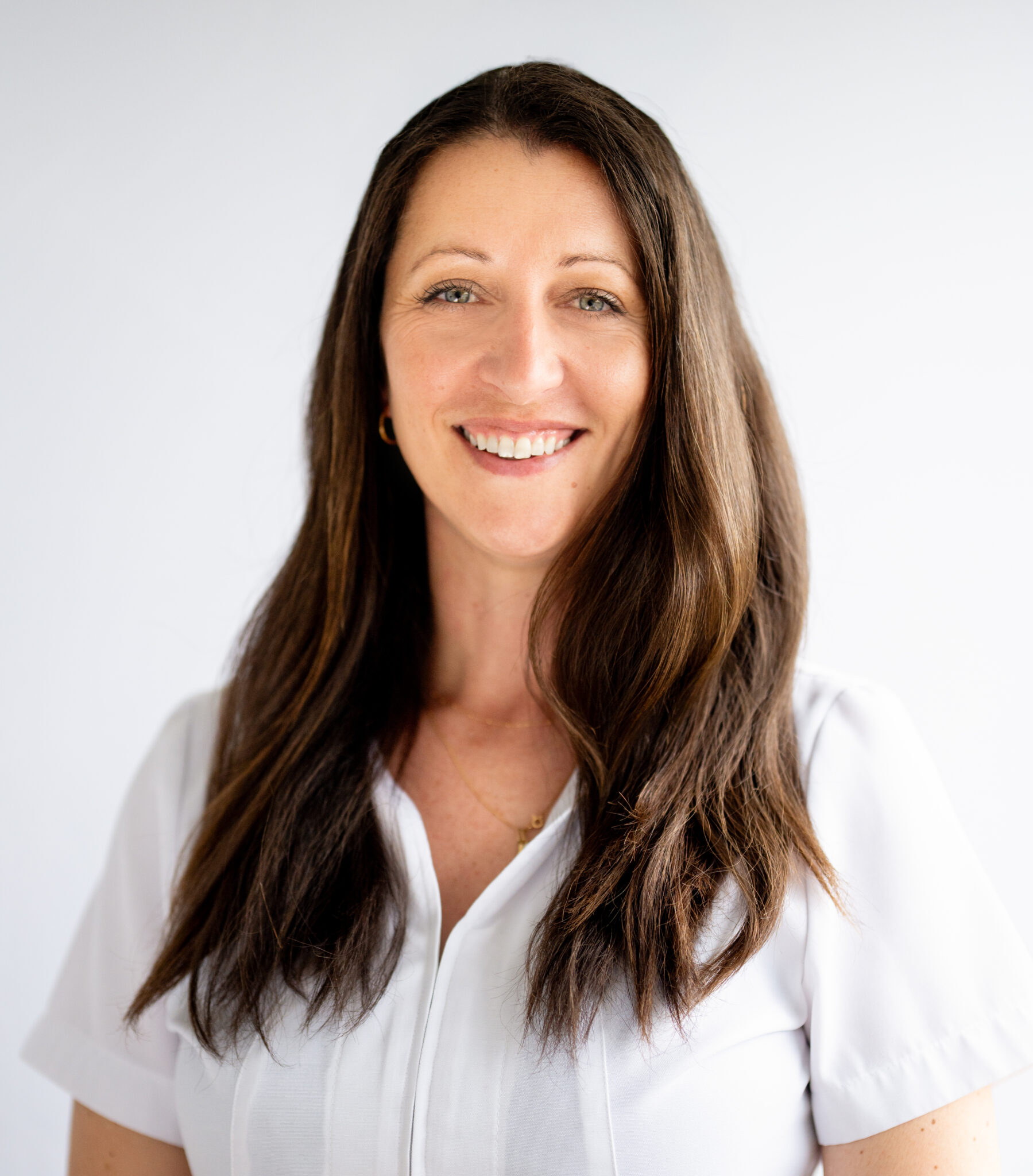 Portrait d’une assistante dentaire souriante aux cheveux longs bruns en blouse blanche